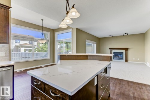 Open concept living area featuring a kitchen island with a light-colored countertop, recessed lighting, and a fireplace with a wooden mantel - 3105 Tredger Place, Edmonton, AB - Indoor Photo Showing Kitchen