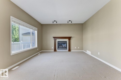 The property offers a living space with a large window, a fireplace with a wooden mantel, and track lighting on the ceiling - 3105 Tredger Place, Edmonton, AB - Indoor With Fireplace