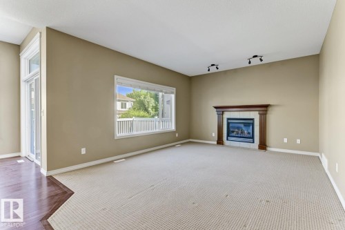 This spacious room features a fireplace with a wood mantle, a large window providing natural light, and sliding glass doors - 3105 Tredger Place, Edmonton, AB - Indoor Photo Showing Living Room With Fireplace