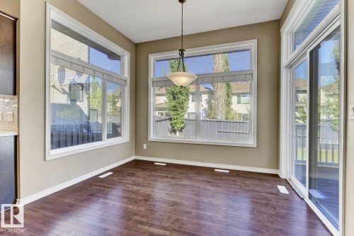 This space features rich hardwood flooring, large windows with roller blinds, and a glass sliding door providing access to an outdoor area - 3105 Tredger Place, Edmonton, AB - Indoor Photo Showing Other Room