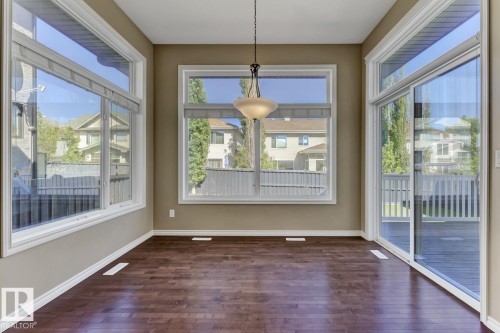 This room features dark wood flooring, expansive windows providing ample natural light, and a sliding glass door that opens to a deck area - 3105 Tredger Place, Edmonton, AB - Indoor Photo Showing Other Room