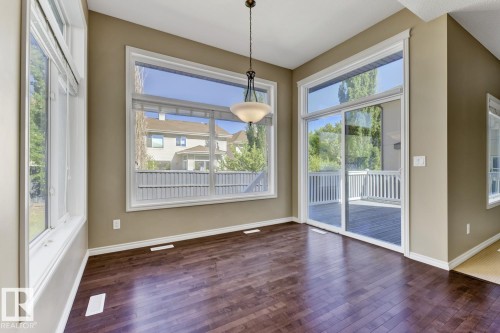 This space features dark hardwood flooring, a modern light fixture, and large windows with white trim - 3105 Tredger Place, Edmonton, AB - Indoor Photo Showing Other Room