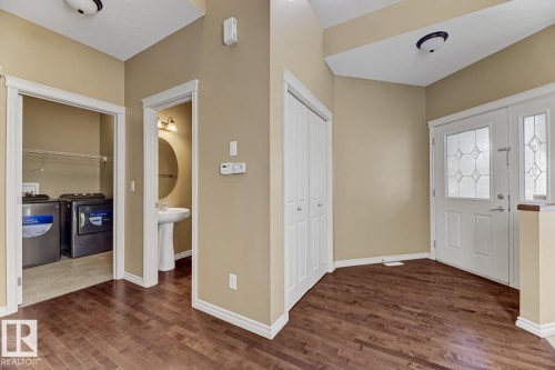 This property features rich hardwood flooring, a front entry door with decorative glass inserts, and a convenient closet with bifold doors - 3105 Tredger Place, Edmonton, AB - Indoor Photo Showing Other Room