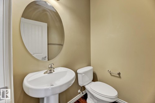 The powder room features a pedestal sink with a chrome faucet, an oval mirror, and a toilet - 3105 Tredger Place, Edmonton, AB - Indoor Photo Showing Bathroom