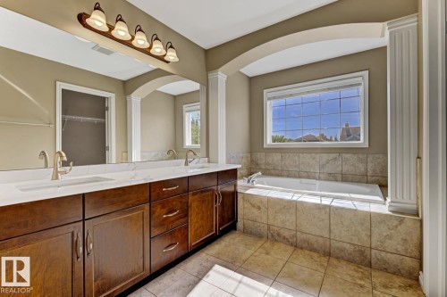 This bathroom features a double vanity with wooden cabinetry, white countertops, and a large mirror - 3105 Tredger Place, Edmonton, AB - Indoor Photo Showing Bathroom