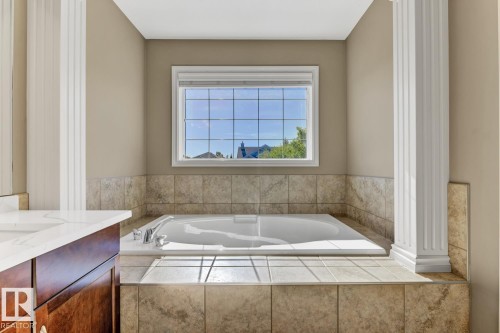 Bathroom featuring an inset bathtub with tiled surround, a large window, and a vanity with a white countertop - 3105 Tredger Place, Edmonton, AB - Indoor Photo Showing Bathroom