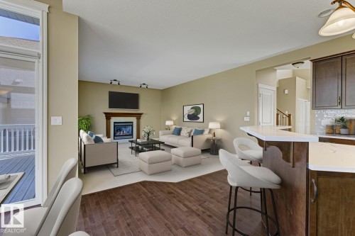 Open-concept living area with a fireplace, hardwood flooring, and a breakfast bar with seating - 3105 Tredger Place, Edmonton, AB - Indoor Photo Showing Living Room With Fireplace