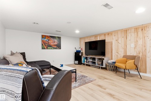 This living area features light-colored plank flooring and a wall with vertical light wood paneling - 18315 68 Avenue, Edmonton, AB - Indoor