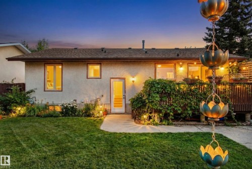 The property features a well-maintained lawn, a spacious deck with string lights, and exterior lighting illuminating the facade and landscaping - 18315 68 Avenue, Edmonton, AB - Outdoor