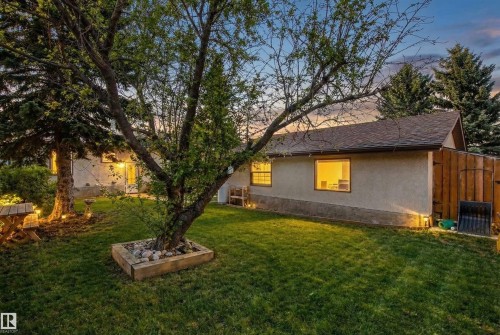 The property features a well-maintained lawn with mature trees and exterior lighting - 18315 68 Avenue, Edmonton, AB - Outdoor
