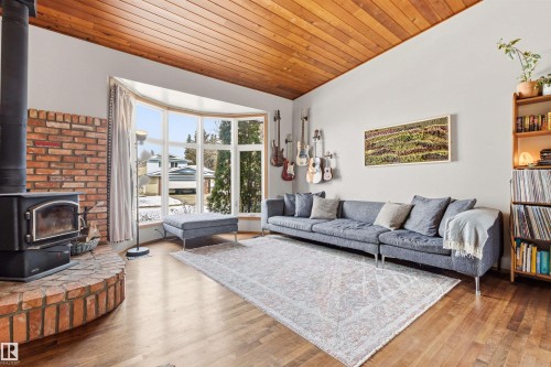 Living room featuring hardwood flooring, a wood-burning stove with a brick surround, and a large bay window - 18315 68 Avenue, Edmonton, AB - Indoor Photo Showing Living Room With Fireplace