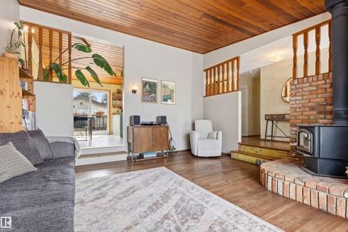 Living area featuring hardwood floors, a wood plank ceiling, and a brick hearth with a wood-burning stove - 18315 68 Avenue, Edmonton, AB - Indoor Photo Showing Living Room