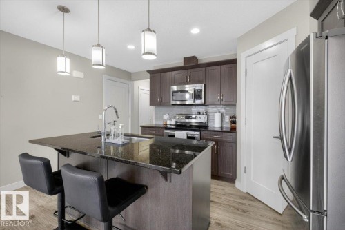 The kitchen features dark wood cabinetry, stainless steel appliances, and a central island with a sink and granite countertops - 16656 14 Avenue, Edmonton, AB - Indoor Photo Showing Kitchen With Stainless Steel Kitchen With Upgraded Kitchen