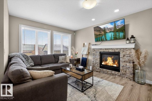 This inviting living space features light-toned walls, recessed lighting, and a contemporary fireplace with a stone surround and a white mantle - 16656 14 Avenue, Edmonton, AB - Indoor Photo Showing Living Room With Fireplace