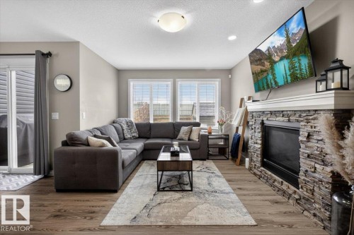 Living area featuring hardwood flooring, a stone-front fireplace with a white mantle, and large windows providing natural light - 16656 14 Avenue, Edmonton, AB - Indoor Photo Showing Living Room With Fireplace