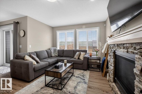 This living space features wood-style flooring, a stone-faced fireplace, and windows with blinds providing natural light - 16656 14 Avenue, Edmonton, AB - Indoor Photo Showing Living Room With Fireplace