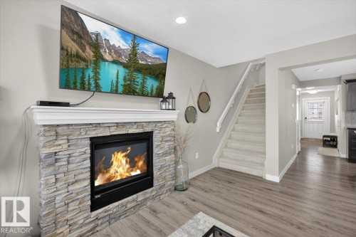 The living area features a fireplace with a stacked stone facade and a white mantel, set against light gray walls - 16656 14 Avenue, Edmonton, AB - Indoor Photo Showing Living Room With Fireplace