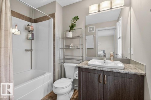 The bathroom features a white bathtub with a shower, a toilet, and a vanity with a white rectangular vessel sink and a granite-style countertop - 16656 14 Avenue, Edmonton, AB - Indoor Photo Showing Bathroom