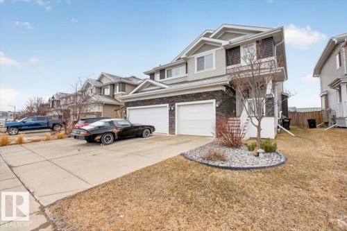 The property features a two-car garage with white doors, a paved driveway, and a front yard with a rock garden and established trees - 16656 14 Avenue, Edmonton, AB - Outdoor