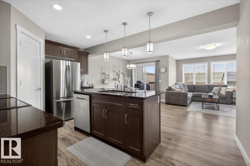 The kitchen features dark cabinetry, stainless steel appliances, and a central island with pendant lighting - 16656 14 Avenue, Edmonton, AB - Indoor Photo Showing Kitchen With Stainless Steel Kitchen With Upgraded Kitchen