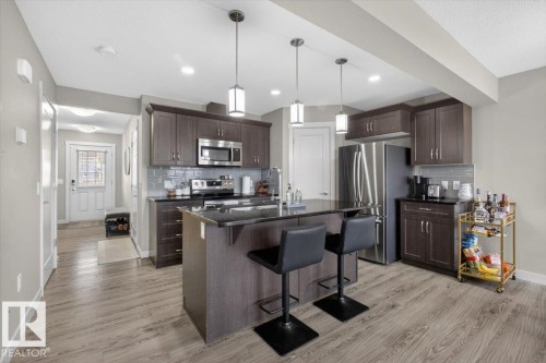 The kitchen features dark wood cabinetry, stainless steel appliances, a center island with seating, and pendant lighting - 16656 14 Avenue, Edmonton, AB - Indoor Photo Showing Kitchen With Stainless Steel Kitchen With Upgraded Kitchen
