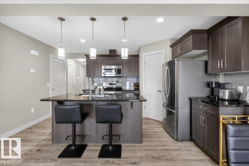 Kitchen featuring dark wood cabinetry, stainless steel appliances, a center island with pendant lighting, and light-colored flooring - 16656 14 Avenue, Edmonton, AB - Indoor Photo Showing Kitchen With Stainless Steel Kitchen With Upgraded Kitchen