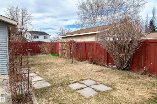 Fenced backyard featuring a lawn area, concrete stepping stones, a decorative metal arbor, and mature landscaping - 1104 35 Street, Edmonton, AB - Outdoor