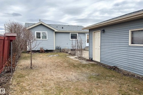 Expansive backyard featuring a red wood fence, a small tree, and a stone path leading to an outbuilding with horizontal siding, an exterior light fixture, and a white door - 1104 35 Street, Edmonton, AB - Outdoor