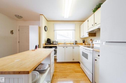 Bright kitchen featuring a wooden island with storage, light wood flooring, white cabinetry, and white appliances - 1104 35 Street, Edmonton, AB - Indoor Photo Showing Kitchen With Double Sink