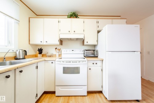 The kitchen features white cabinetry, a white electric range, and a white refrigerator, complemented by light-toned countertops and wood flooring - 1104 35 Street, Edmonton, AB - Indoor Photo Showing Kitchen