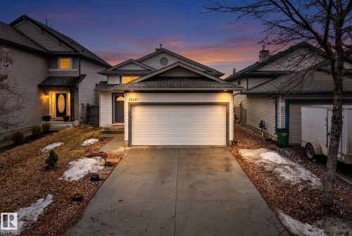 The property features a concrete driveway leading to an attached garage, a walkway to the main entrance, and exterior lighting illuminating the front of the home - 20147 48 Avenue, Edmonton, AB - Outdoor