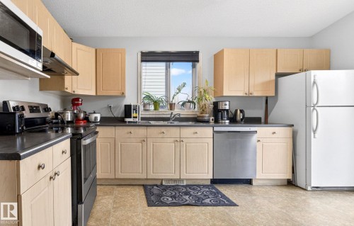 The kitchen features light-toned cabinetry, dark countertops, a stainless steel dishwasher, and a window with blinds - 20147 48 Avenue, Edmonton, AB - Indoor Photo Showing Kitchen With Double Sink