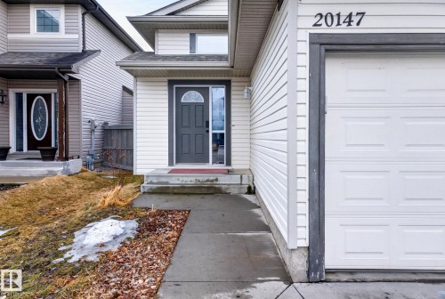 The property features a white paneled exterior, a dark gray front door with an arched window, and a white paneled garage door - 20147 48 Avenue, Edmonton, AB - Outdoor