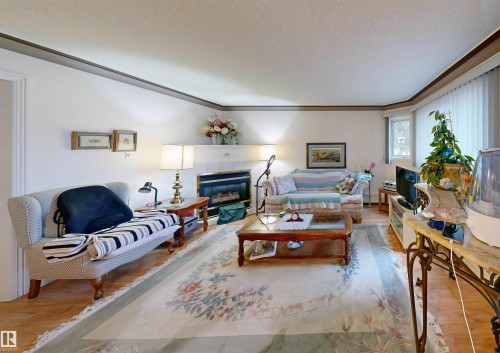 Living area featuring hardwood flooring, a fireplace with a tile surround, and a bay window with vertical blinds - 31 9914 80 Avenue, Edmonton, AB - Indoor Photo Showing Living Room With Fireplace