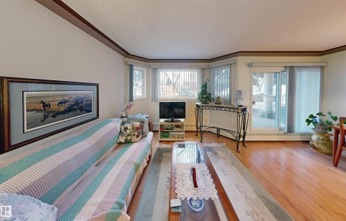 The living area features hardwood flooring, a large bay window, and a sliding glass door providing external access - 31 9914 80 Avenue, Edmonton, AB - Indoor Photo Showing Living Room With Fireplace