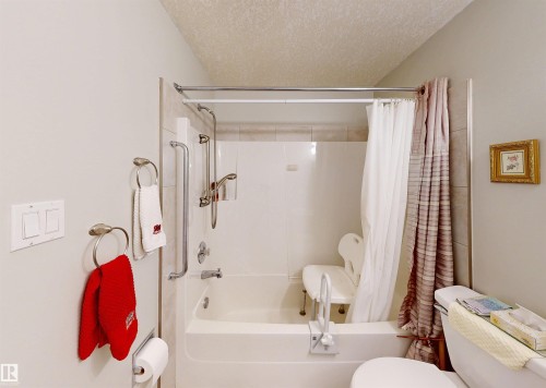 Bathroom featuring a white bathtub with a shower, a shower curtain, and wall-mounted handrails - 31 9914 80 Avenue, Edmonton, AB - Indoor Photo Showing Bathroom