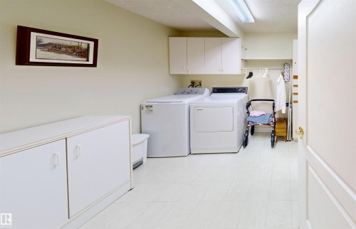 Utility room featuring a washer and dryer, white cabinetry, a built-in shelf with hanging rod, and light-colored flooring - 31 9914 80 Avenue, Edmonton, AB - Indoor Photo Showing Laundry Room