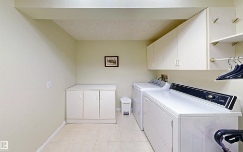 Laundry room featuring tiled flooring, a built-in storage cabinet, and overhead cabinetry with shelving and a hanging rod - 31 9914 80 Avenue, Edmonton, AB - Indoor Photo Showing Laundry Room