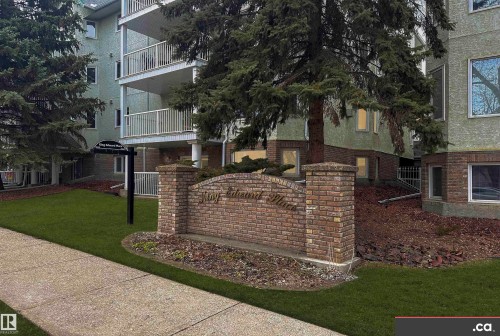 The property features a brick signage with an arched top, set against a backdrop of mature trees and a manicured lawn - 31 9914 80 Avenue, Edmonton, AB - Outdoor With Balcony