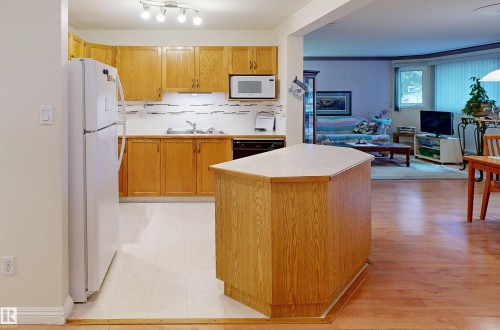 The kitchen features light wood cabinetry, a white refrigerator, and a kitchen island with a light-colored countertop - 31 9914 80 Avenue, Edmonton, AB - Indoor Photo Showing Kitchen With Double Sink