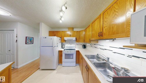 The kitchen features light wood cabinetry, white appliances, a double basin stainless steel sink, and a white subway tile backsplash with dark accent lines - 31 9914 80 Avenue, Edmonton, AB - Indoor Photo Showing Kitchen