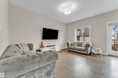 The living area features hardwood floors and a window providing natural light, alongside a door leading to a balcony with dark railings - 32 1703 16 Avenue, Edmonton, AB - Indoor Photo Showing Living Room