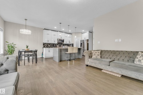 Open concept living area featuring light-toned hardwood flooring, a kitchen with white cabinetry and a patterned backsplash, and a dining area with a modern chandelier - 32 1703 16 Avenue, Edmonton, AB - Indoor Photo Showing Living Room