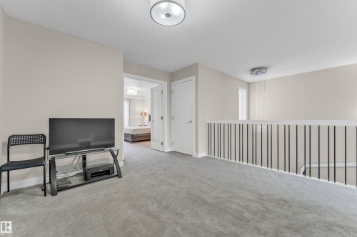 This space features light-colored walls, gray carpeting, and a white railing with black balusters - 32 1703 16 Avenue, Edmonton, AB - Indoor Photo Showing Other Room