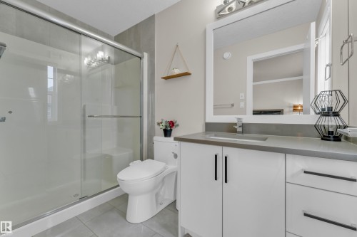 The bathroom features a spacious shower with glass sliding doors, a modern vanity with a rectangular sink and dark countertop, and a white framed mirror - 32 1703 16 Avenue, Edmonton, AB - Indoor Photo Showing Bathroom