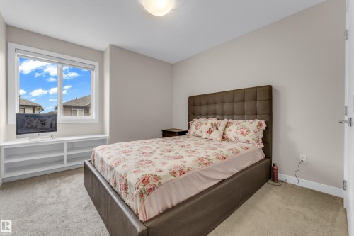 A bright room featuring a window with a view of residential roofs and blue sky, built-in shelving, and light-colored carpet - 32 1703 16 Avenue, Edmonton, AB - Indoor Photo Showing Bedroom