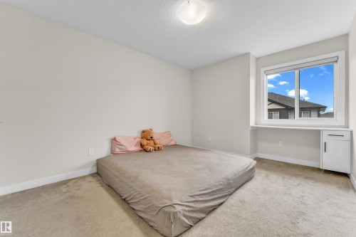Bedroom featuring light-colored carpet, a window with a view of rooftops and a blue sky, and a built-in desk area with a cabinet - 32 1703 16 Avenue, Edmonton, AB - Indoor Photo Showing Bedroom