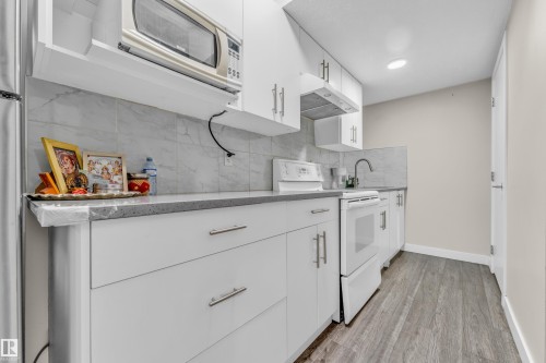 The kitchen features white cabinetry, a microwave, a range, and a sink with a faucet - 32 1703 16 Avenue, Edmonton, AB - Indoor Photo Showing Kitchen