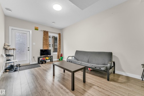 Living area featuring wood-look flooring, light-colored walls, and a window with curtains - 32 1703 16 Avenue, Edmonton, AB - Indoor Photo Showing Living Room