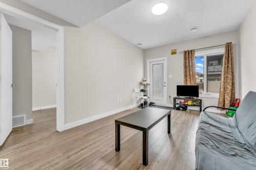 The living area features light-toned walls, wood-look flooring, and a large window with privacy curtains - 32 1703 16 Avenue, Edmonton, AB - Indoor Photo Showing Living Room